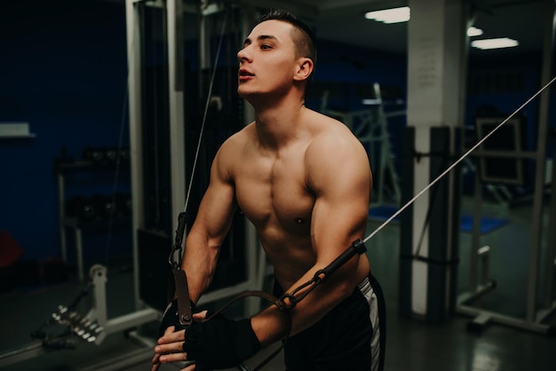 Un hombre ejerciendo trx de entrenamiento de suspensión en el gimnasio oscuro