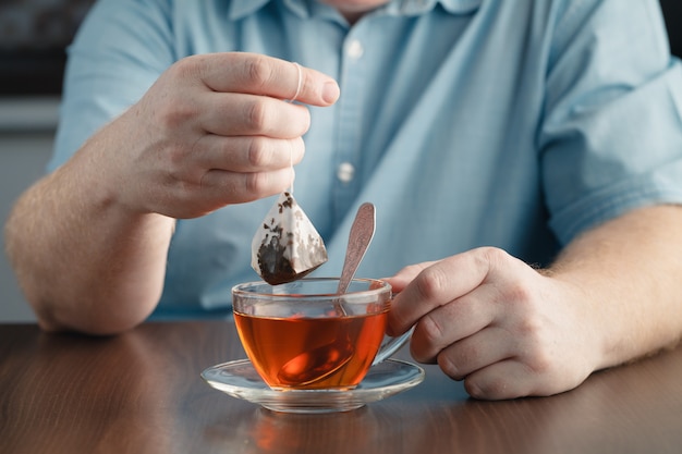 Hombre elaborando bolsita de té con un vaso de té en la mesa en la oficina