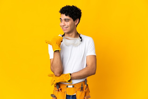 Hombre electricista venezolano aislado en amarillo apuntando hacia el lado para presentar un producto