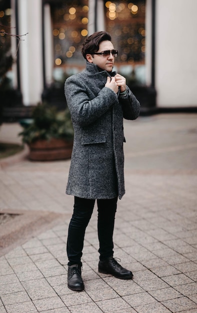 hombre elegante con un abrigo gris y gafas de sol caminando por la ciudad.