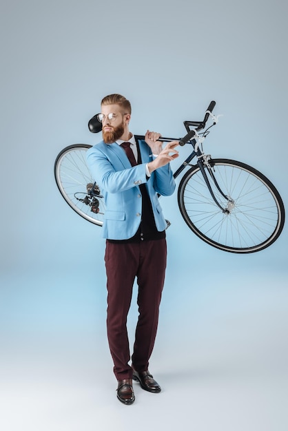 Hombre elegante en anteojos y traje con bicicleta aislado en azul