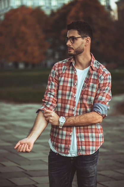 Hombre elegante con barba y gafas de sol de pie en el parque.