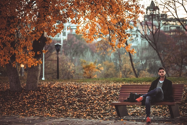 Hombre elegante con barba y gafas de sol de pie en el parque.