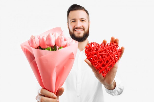 Hombre elegante con barba, con un ramo de tulipanes rosados y un corazón rojo de San Valentín, un regalo para el Día de San Valentín