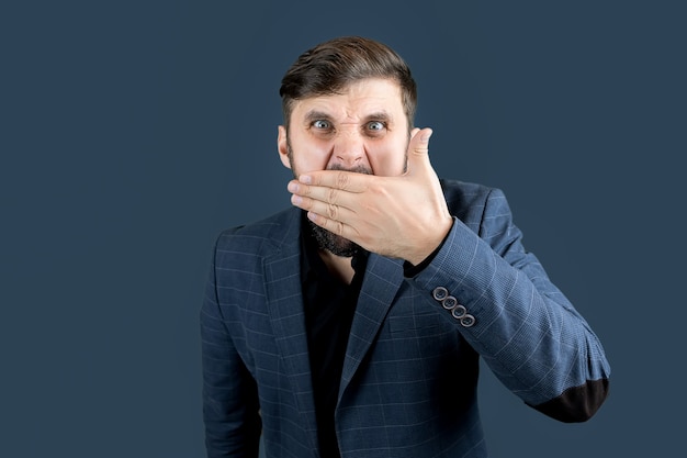 Un hombre elegante con barba con un traje azul se tapó la boca con la mano