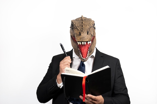 Hombre elegante con cabeza de T Rex pensando en escribir sus ideas en su planificador sobre un fondo blanco