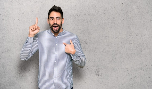 Hombre elegante con camiseta con expresión facial sorpresa sobre muro texturizado.