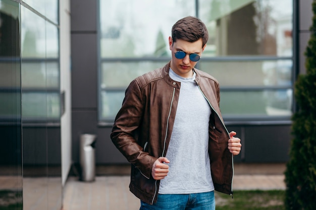 Un hombre elegante con chaqueta de cuero, gafas y camiseta gris. Foto de la calle