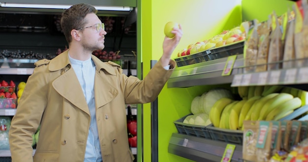 Hombre elegante elige manzanas en el supermercado Alimentos saludables cítricos Hombre seleccionando manzanas frescas en el departamento de productos de la tienda de comestibles