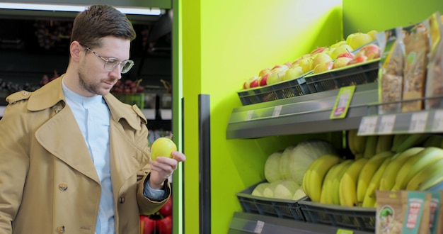 Hombre elegante elige manzanas en el supermercado Alimentos saludables cítricos Hombre seleccionando manzanas frescas en el departamento de productos de la tienda de comestibles