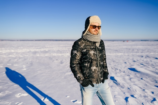 Hombre elegante con gafas de sol posando en el campo nevado