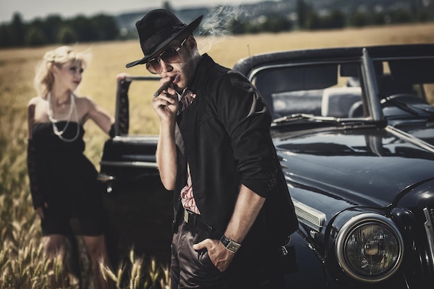 Hombre elegante con gafas de sol y su novia cerca del auto en el campo