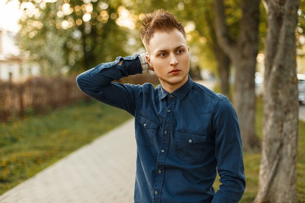 Hombre elegante joven guapo con una camisa azul posando en el parque en un día soleado