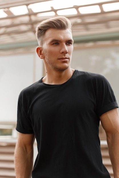 Hombre elegante modelo guapo con peinado en camiseta negra en la calle de la ciudad