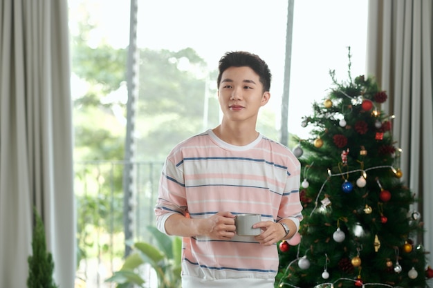 Hombre elegante con rostro emocional positivo posando con una taza de café con adornos de árbol de navidad y año nuevo