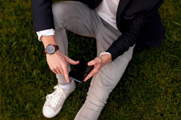 Hombre elegante sentado en la hierba y con smartphone