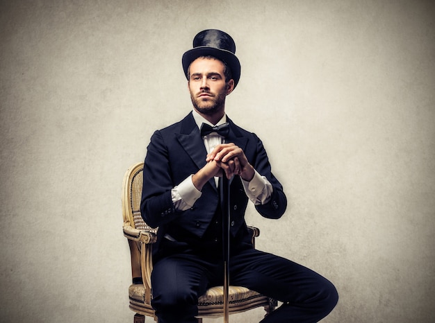 Hombre elegante con sombrero de copa y sentado en una silla