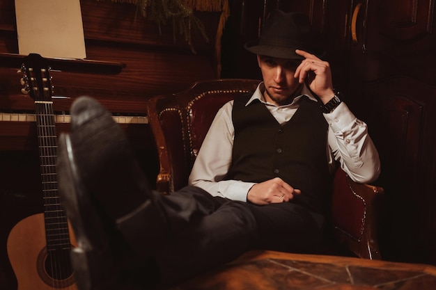 Un hombre elegante con sombrero está sentado en un sillón en un elegante interior retro del restaurante