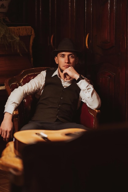 Un hombre elegante con sombrero está sentado en un sillón en un elegante interior retro del restaurante