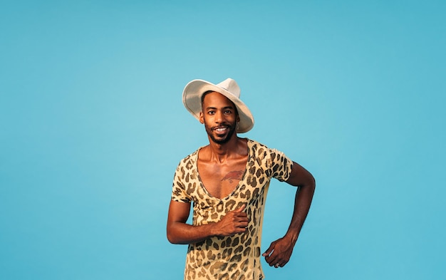 Hombre elegante con sombrero de paja bailando en el estudio y mirando a la cámara con fondo azul