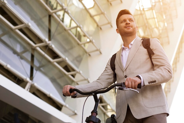 Hombre elegante sonriente mirando a un lado y sosteniendo un manillar de su bicicleta