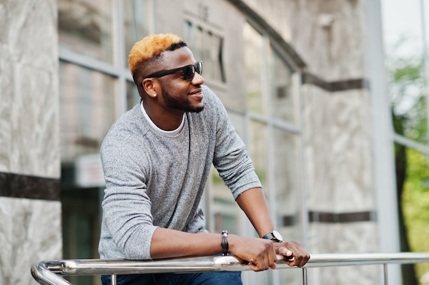 Hombre elegante con suéter gris y gafas de sol negras posadas en la calle