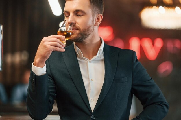 Un hombre elegante con traje negro está en el bar probando la bebida alcohólica.
