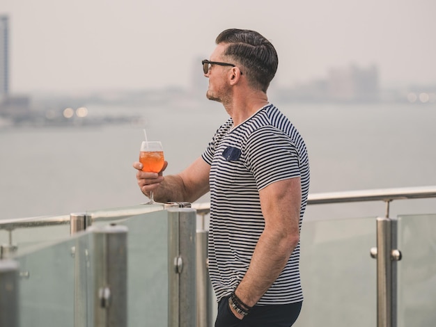 Hombre elegante con un vaso de bebida de pie en la cubierta vacía