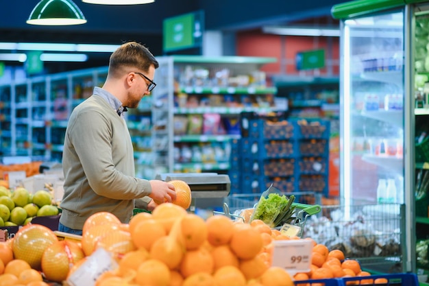 Un hombre elige frutas en un supermercado con un carrito de compras