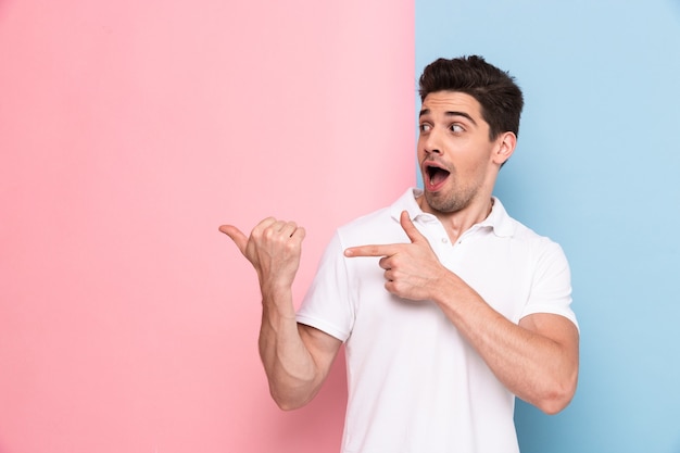 Hombre emocionado en camiseta casual sonriendo y mostrando copyspace en su palma, aislado sobre pared colorida