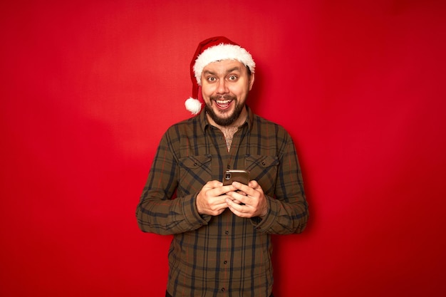 un hombre emocionado feliz en el sombrero de Navidad de Santa Claus con el teléfono en sus manos se regocija de la sensación recibida
