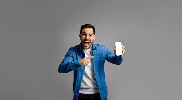 Hombre emocionado gritando y señalando la pantalla del teléfono inteligente con fondo gris