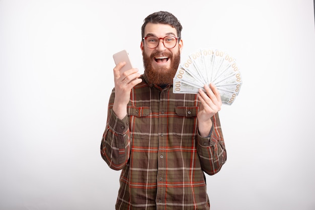 Foto el hombre emocionado está mostrando un montón de dinero y su teléfono en blanco.