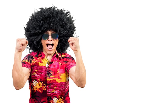 Hombre emocionado con peluca afro funky y elegantes gafas de sol apretando los puños y gritando mientras celebra el éxito contra el fondo blanco