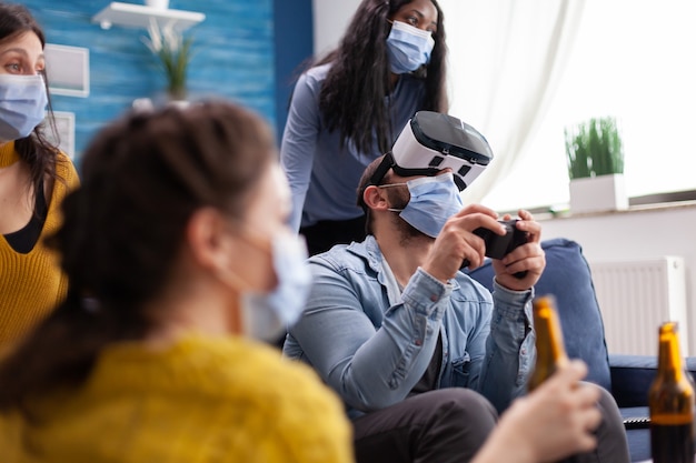 Hombre emocionado que pasa tiempo con amigos que experimentan la realidad virtual jugando juegos con auriculares vr con máscara facial para evitar la propagación del coronavirus en tiempos de pandemia social.