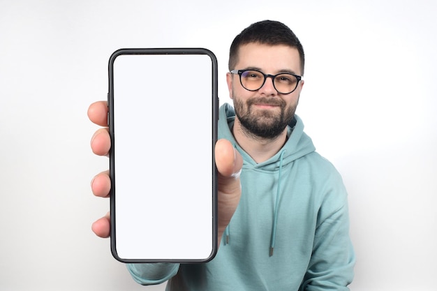 Hombre emocional alegre que sostiene el teléfono celular en blanco grande en la mano que muestra la pantalla blanca