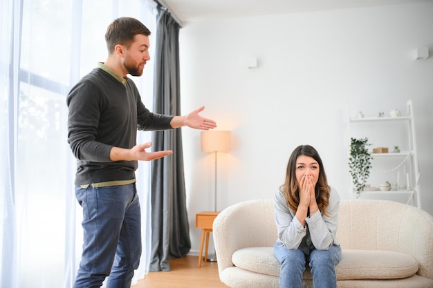 Hombre emocional gesticulando y gritando a su esposa pareja joven que tiene una pelea en casa concepto de abuso doméstico