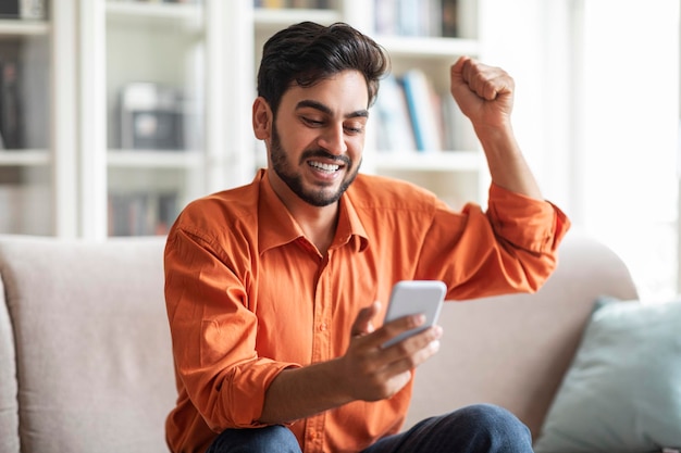 Hombre emocional del medio oriente usando teléfono inteligente y gesticulando