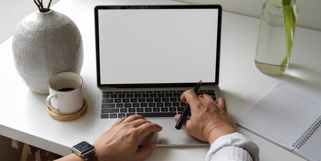 Hombre empresario trabajando con la computadora portátil en el escritorio de oficina blanco con agenda en blanco, decoraciones y taza de café