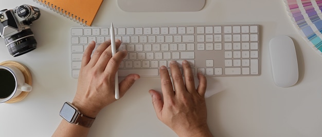 Hombre empresario trabajando con el portátil en el escritorio de oficina blanco con computadora, cámara y taza de café