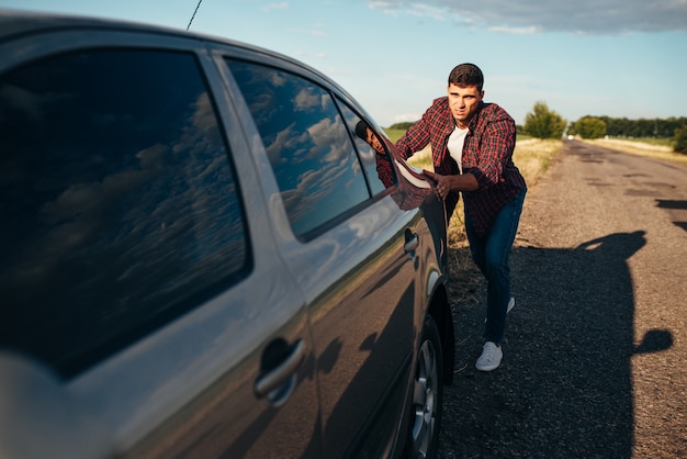 Hombre empujando el coche roto. vehículo con trounble en carretera en día de verano