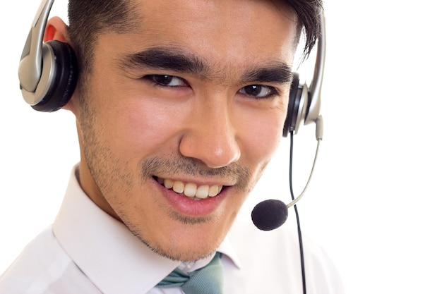 Hombre encantador joven con cabello negro en camisa blanca con corbata azul usando auriculares sobre fondo blanco en estudio