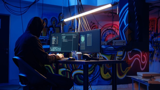 Hombre encapuchado en escondite subterráneo hackeando computadoras