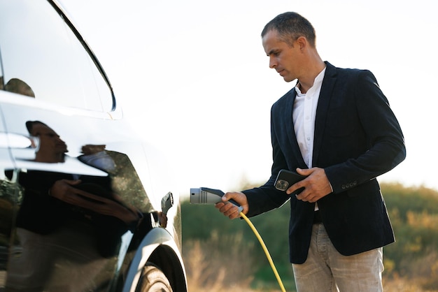 hombre enchufando el coche eléctrico de la estación de carga hombre enchufando el cable de alimentación al coche eléctrico