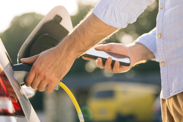 Hombre enchufando el coche eléctrico de la estación de carga macho conectando el cable de alimentación al coche eléctrico