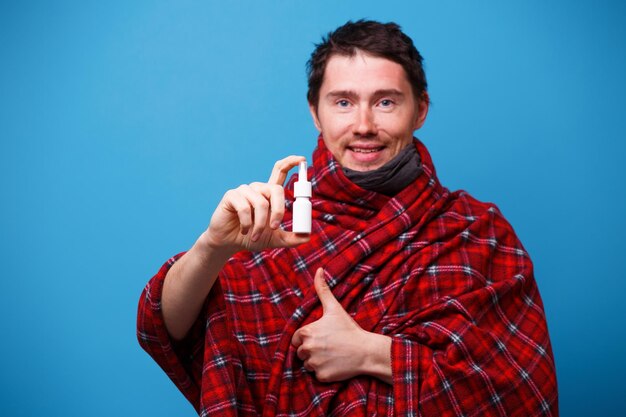 Un hombre enfermo envuelto en una manta está de pie con un aerosol nasal en la mano