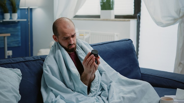 Hombre enfermo leyendo la etiqueta de la botella con pastillas y medicamentos