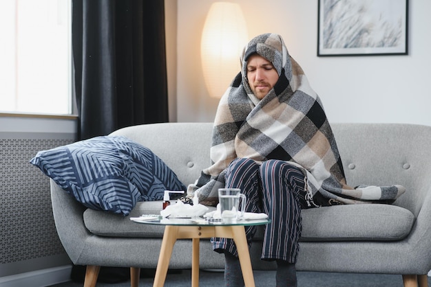 Un hombre enfermo se sienta en casa en un sofá gris con una manta Protección contra enfermedades coronavirus enfermedad gripe