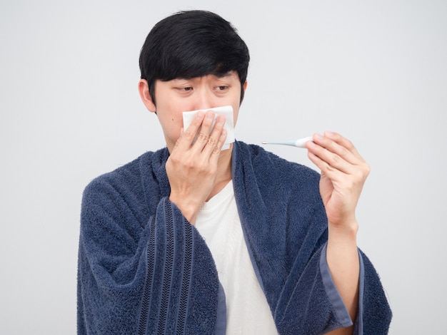Hombre enfermo sosteniendo un pañuelo en la nariz y mirando el termómetro en la mano sintiéndose triste