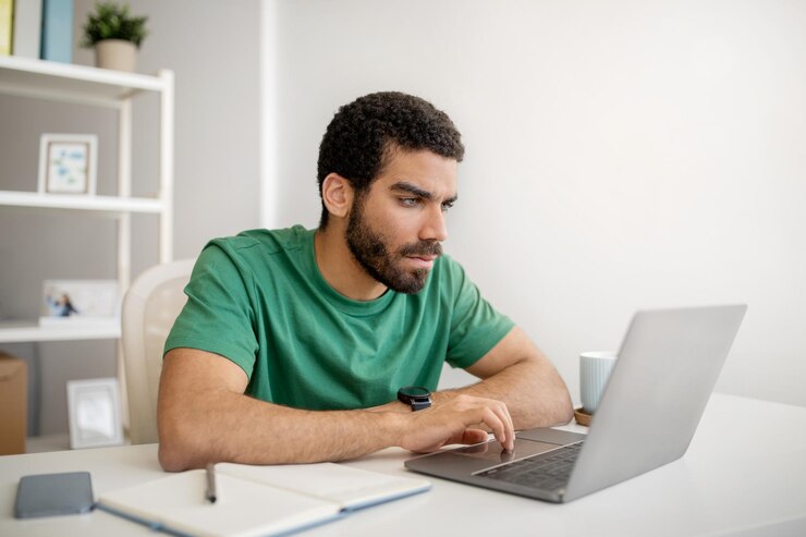 Foto hombre enfocado con barba en camiseta verde trabajando atentamente en una computadora portátil en un brillante